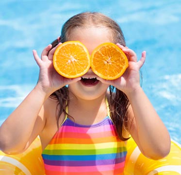 Girl holding up orange slices covering her eyes